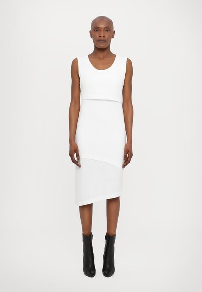 Rochie midi albă cu un design cu decupaj, bretele fără mâneci și tiv asimetric. Asortată cu cizme negre până la gleznă.