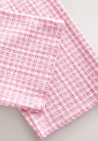 Țesătură roz și albă în carouri, cu suprafață texturată, prezentând un model în grilă și o cădere moale a materialului.