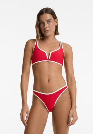 Červený bikini set obsahující top s v-výstřihem a bílým lemem, doplněný o nízké kalhotky. Hladký, elastický materiál s klasickým střihem.