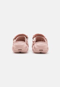 Pink clogs with a smooth texture, back straps, ventilation holes, and a rounded shape. The sole features a wave-like design for grip.