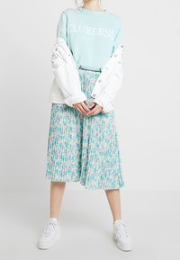 Ljusblå tröja med texten "CLUELESS", vit plisserad blommig kjol, vit denimjacka och vita sneakers. Detaljerat blommönster på kjolen.