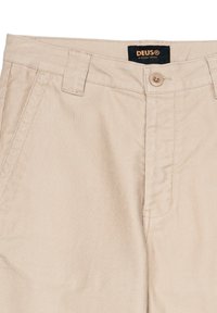 Pantaloni beige in tessuto di cotone, dotati di chiusura con bottone, passanti per cintura e tasche laterali con una finitura liscia e testurizzata.