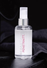 Heldere fles met Sebastian Penetraitt serum met een witte pomp, gelabeld met vetgedrukte roze en zilveren tekst, rustend op een donkere, gestructureerde handdoek.