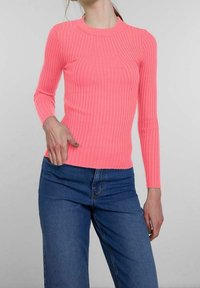 Figurbetontes, langärmliges Rippoberteil in leuchtendem Pink. Rundhalsausschnitt, strukturierter Stoff, kombiniert mit hochgeschnittenen blauen Jeans.
