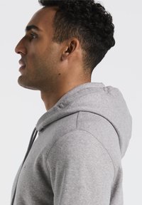 Grijze hoodie met een zachte textuur, geribde manchetten en een eenvoudig ontwerp. Inclusief een trekkoord in de capuchon en een subtiele logo op de borst.