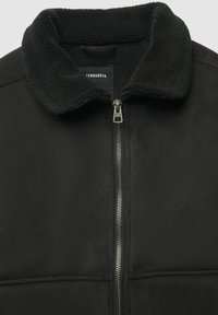 Giacca nera con zip, dotata di un colletto soffice, realizzata in materiale morbido. Presenta una zip completa e dettagli di cucitura orizzontale. Etichetta del marchio visibile.