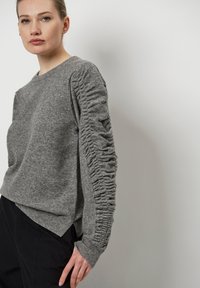 Grijze trui van zacht materiaal, met gathered details op de mouwen, geribbelde boorden en een relaxte pasvorm.