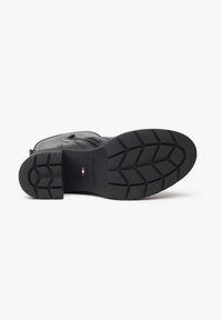 Botte en cuir noir avec une semelle en caoutchouc texturée, présentant un motif strié pour l'adhérence et une fermeture éclair sur le côté pour un enfilage facile.
