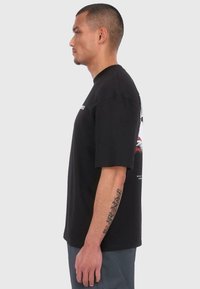 Black cotton t-shirt featuring short sleeves, a crew neck, and a graphic design on the back. Cut in a relaxed fit.