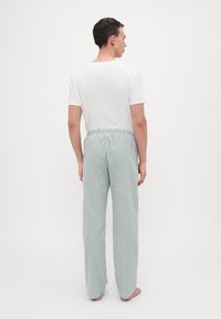 T-shirt blanc et pantalon de pyjama à carreaux verts. Le pantalon présente une taille élastique et des jambes droites, fabriqué en tissu doux et respirant.