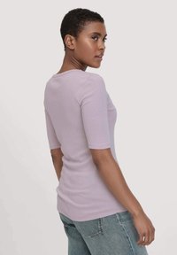 Licht lavendelkleurig shirt met korte mouwen en een ronde halslijn. Glad van textuur, aansluitend ontwerp, gecombineerd met hooggerijpte blauwe jeans.