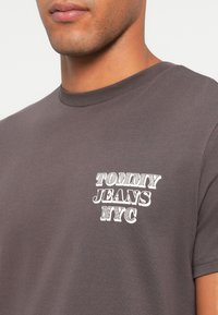 Szary bawełnowy t-shirt z okrągłym dekoltem i krótkim rękawem, ozdobiony białym napisem "TOMMY JEANS NYC" na lewej piersi.