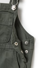 Donkergroene overall met een gestructureerde stof, verstelbare banden, zilverkleurige hardware en een voorzak met knoopdetails.