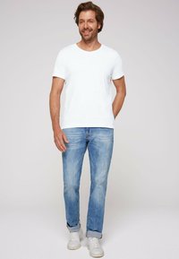 White crew-neck t-shirt paired with light blue jeans and white sneakers. Casual fit with rolls at the jeans' hem and a relaxed appearance.