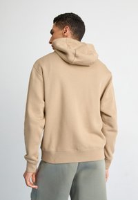 Sweatshirt bege com capuz, textura suave, punhos e bainha canelados, corte descontraído, combinado com calções verde claro.