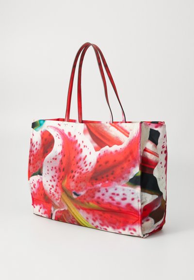 Tasche mit einem lebhaften Druck von rosa und weißen Lilien, roten Kunstledergriffen und einer strukturierten rechteckigen Form.