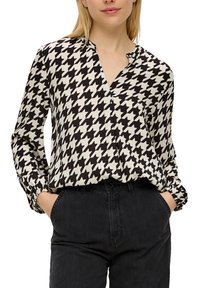 Zwart-wit geblokte blouse met een V-hals en lange, gathered mouwen. Gecombineerd met donkere spijkerbroeken.