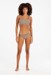 Pruhovaný bikini s crop topem s čtvercovým výstřihem a širokými ramínky, doplněný o vysoké spodní díly. Barvy zahrnují modrou, červenou, žlutou a béžovou.