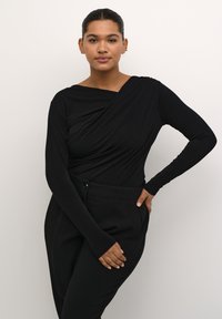 Haut noir à manches longues avec un design drapé et un large col. Associé à un pantalon noir ajusté taille haute, créant un look cohérent.