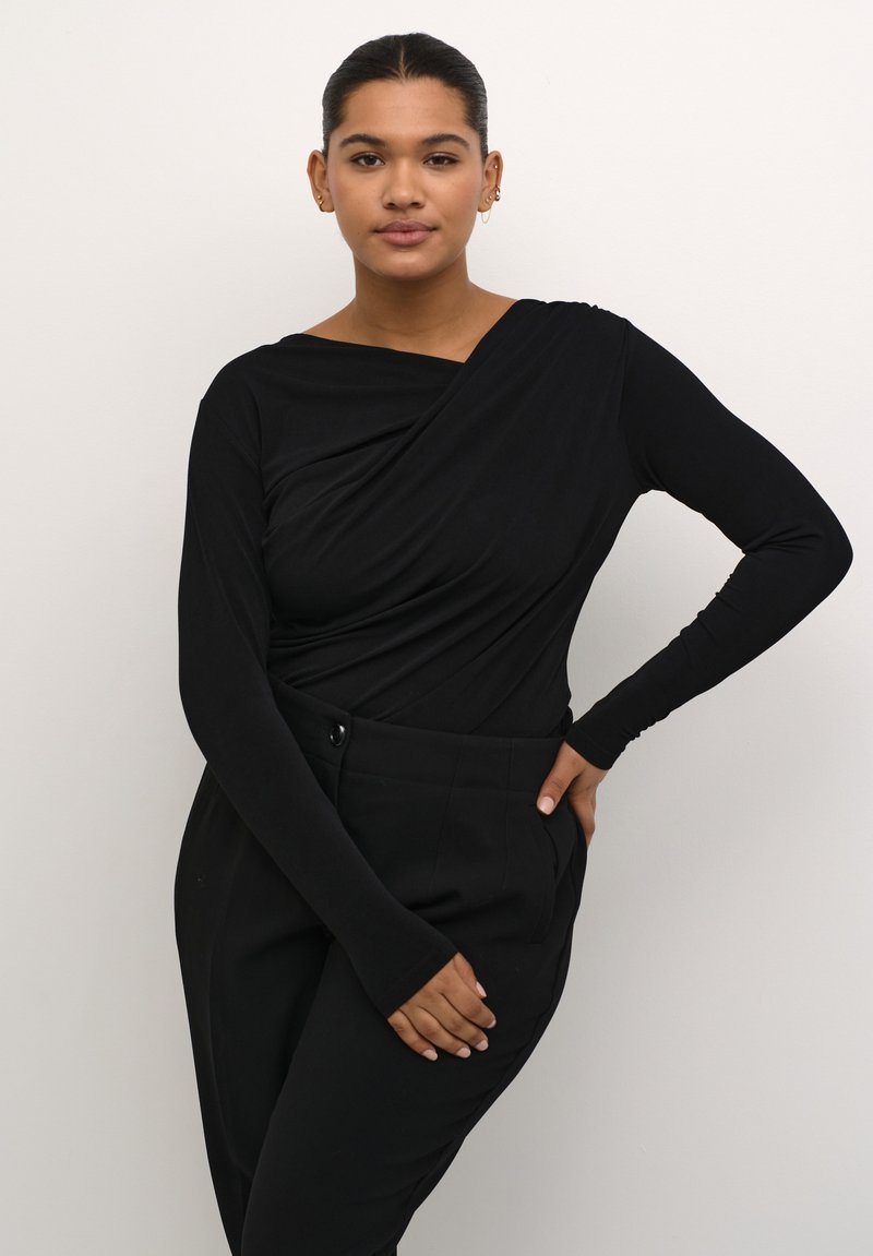 Haut noir à manches longues avec un design drapé et un large col. Associé à un pantalon noir ajusté taille haute, créant un look cohérent.