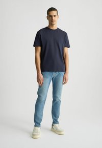 Maglietta a maniche corte blu navy abbinata a jeans azzurri e sneakers bianche. La maglietta presenta un collo rotondo e un dettaglio logo discreto.
