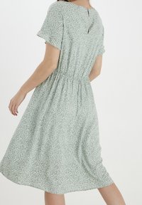 Robe fleurie verte à manches courtes, taille élastique, ourlet au genou et détail en forme de trou de serrure au dos. Tissu léger avec un motif texturé.