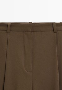 Hnědé látkové kalhoty s hladkou texturou, s plochým předním dílem, záhyby a poutky na opasek v pase. Žádné viditelné kapsy nejsou zobrazeny.