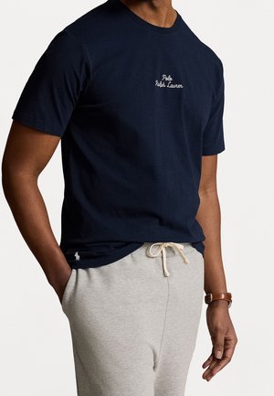 Navy Baumwoll-T-Shirt mit Rundhalsausschnitt, mit weißem gesticktem Text "Polo Ralph Lauren." Kombiniert mit hellgrauen Sweatpants im lässigen Schnitt.
