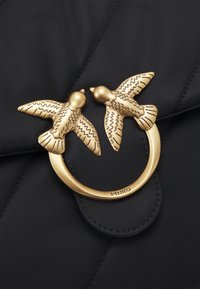 Borsa in tessuto trapuntato nero con una chiusura in metallo dorato a forma di due uccelli che si fronteggiano, dettagliata con incisioni sulle loro ali.