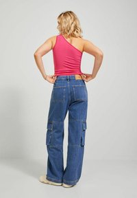 Top de tirantes fucsia de un solo hombro combinado con pantalones cargo de denim azul holgados que cuentan con múltiples bolsillos y una etiqueta de cuero marrón en la parte trasera.