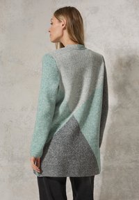 Lange cardigan van een zacht wolmengsel in grijs, lichtgrijs en teal. Heeft een geometrisch kleurbloks ontwerp en een open voorkant. Gek textureerd oppervlak.