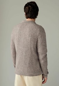 Pulover tricotat într-o nuanță deschisă de taupe, cu textură în relief, având un guler clasic și mâneci lungi. Material neted, croială ajustată.