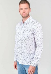 Witte overhemdd met een bloemenpatroon in blauw, voorzien van een klassieke kraag en lange mouwen. Gemaakt van lichtgewicht stof.