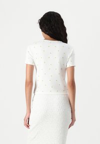 Witte top met korte mouwen, met een geribbelde textuur en kleine gele bloemenpatronen. Cropped ontwerp, ronde halslijn. Gecombineerd met een gestructureerde rok.