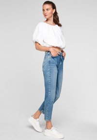 Jeansy z wysokim stanem w niebieskim kolorze o prostym kroju nogawek, w połączeniu z białym topem crop z bufiastymi rękawami i białymi trampkami. Gładka tekstura denimu.