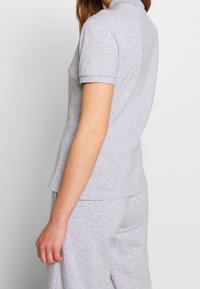 Polo gris en coton avec un col à revers et des manches courtes, présentant une coupe décontractée et une texture lisse. Porté avec un short gris assorti.