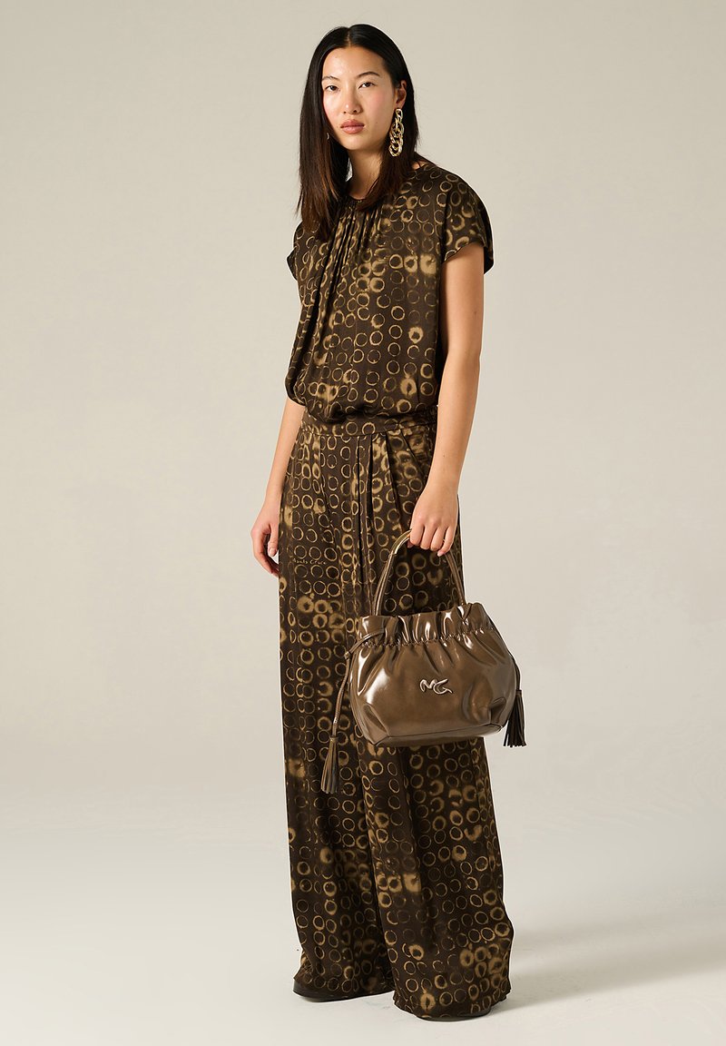 Outfit marrone a fantasia con motivi circolari; top largo e pantaloni a gamba larga. Accessorio: borsa marrone a mano con frange.
