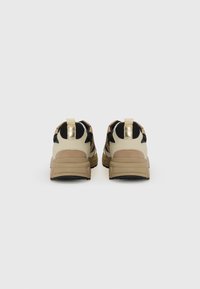 Beige and black sneakers with a textured finish, featuring gold accents and a cushioned sole. Rear view shows sturdy pull tabs for easy wear.