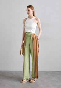 White cropped tank top, green trousers with vertical multi-colored stripes, and tan platform sandals. Features a drawstring waist and side pockets.