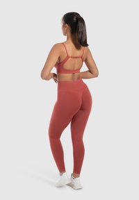 Soutien-gorge de sport actif rouge avec un dos découpé et des accessoires ajustables, associé à un legging taille haute assorti, présentant une texture lisse.