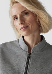 Grey zip-up jacket with a stand-up collar, made of textured fabric, featuring a front zipper and a subtle sparkle finish.