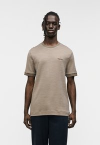 Μπεζ κοντομάνικη μπλούζα με υφή και ριμπ λαιμόκοψη. Μικρό λογότυπο στο αριστερό στήθος. Χαλαρή εφαρμογή.