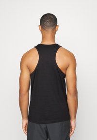 Camiseta sin mangas negra con cuello redondo y amplias sisas. Hecha de una tela suave, diseño ajustado, lisa sin patrones ni acentos.