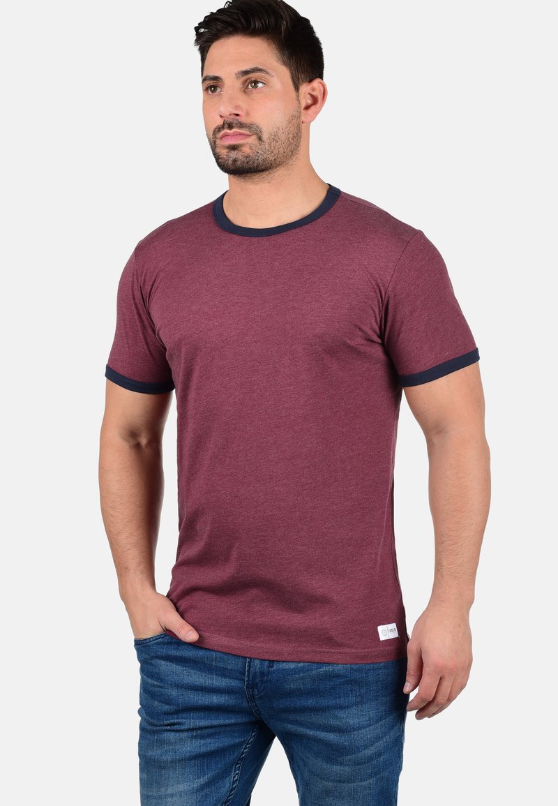 Bordo spalvos medvilnės marškinėliai su tamsiai mėlynu gumuliniu apykakle ir rankovėmis. Trumpomis rankovėmis, pritaikyta forma ir mažas logotipas apatineje dalyje.