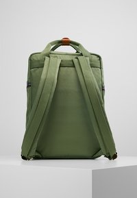 Zelený látkový batoh s nastavitelnými polstrovanými popruhy, horní rukojetí a zipovou kapsou. Hladký povrch a minimalistický design.