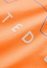 Oranžs kokvilnas audums ar plakanu tekstūru. Satur baltus un zilos grafiskos tekstus un kontūras modernā fonta stilā.