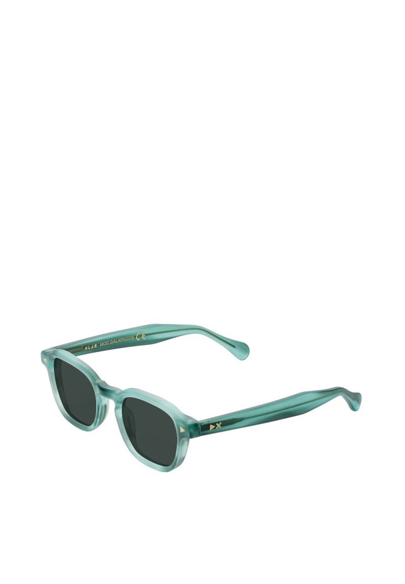 Un paio di occhiali da sole quadrati, traslucidi, di colore teal con lenti scure e dettagli dorati sulle astine, con la scritta "XLAB MOD GALAPAGOS."