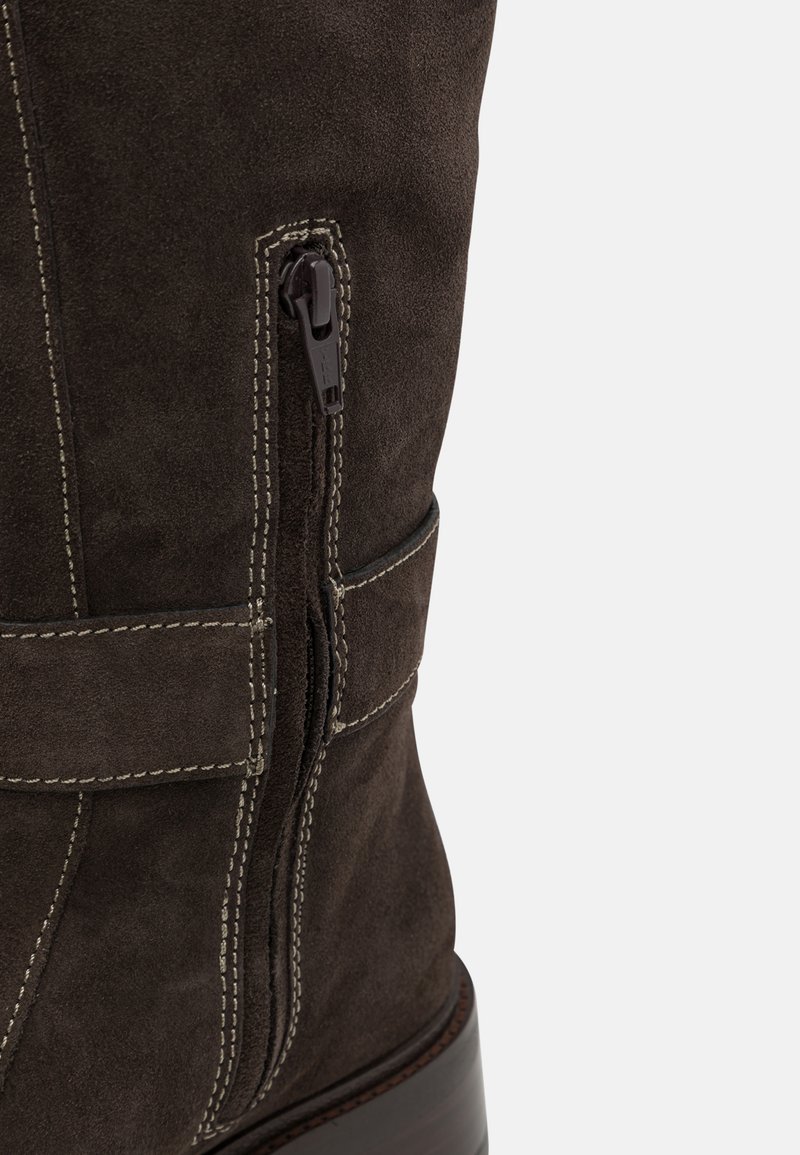 Bruine suède enkellaars met een zijrits, contrasterende witte stiksels en een stevige houten hak. Beschikt over een klittenband detail.