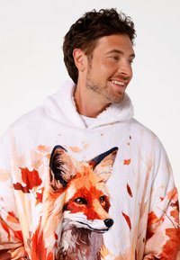 Wegwerpkleed met kap van zacht wit materiaal met een realistisch vosontwerp in oranje en bruine accenten, omgeven door herfstbladeren.