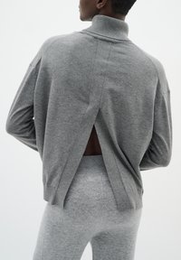 Gray knit sweater with a high collar, featuring a split at the back, paired with matching gray leggings. Soft texture, relaxed fit.